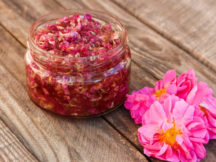 Jam jar of rose petals on wooden background.